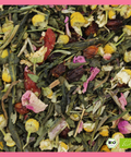 Eine detaillierte Makroaufnahme der "So Damn Pretty" Grünteemischung mit grünen Teeblättern, leuchtend gelben Kamillenblüten, rosa Rosenblüten und dunkelroten Fruchtstücken (Goji-Beeren). Unten rechts ist das BIO-Siegel eingeblendet.