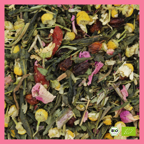 Eine detaillierte Makroaufnahme der "So Damn Pretty" Grünteemischung mit grünen Teeblättern, leuchtend gelben Kamillenblüten, rosa Rosenblüten und dunkelroten Fruchtstücken (Goji-Beeren). Unten rechts ist das BIO-Siegel eingeblendet.