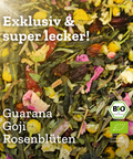 Eine Nahaufnahme der beleuchteten "So Damn Pretty" Grünteemischung, mit sichtbaren Zutaten wie Guarana, Goji-Beeren, Rosenblüten und Kamille. Text-Overlays bewerben den Tee als "Exklusiv & super lecker!" und zeigen das BIO-Siegel.