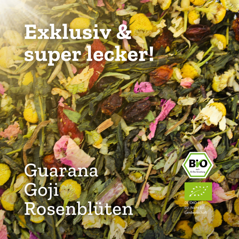 Eine Nahaufnahme der beleuchteten "So Damn Pretty" Grünteemischung, mit sichtbaren Zutaten wie Guarana, Goji-Beeren, Rosenblüten und Kamille. Text-Overlays bewerben den Tee als "Exklusiv & super lecker!" und zeigen das BIO-Siegel.