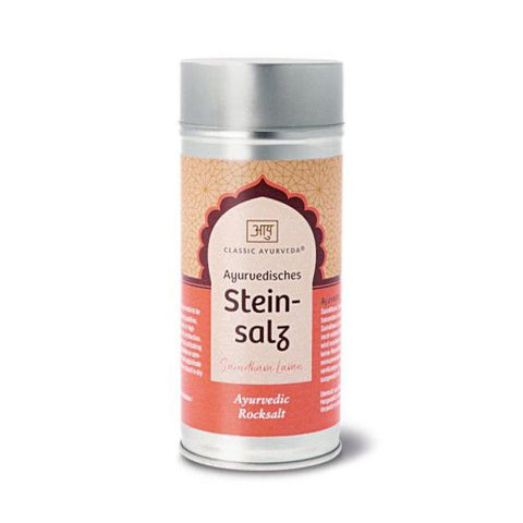 Ein hoher silberner Streuer von „Classic Ayurveda“ mit „Ayurvedischem Steinsalz“, versehen mit einem pfirsich- und weinroten Etikett mit dekorativem Bogenrahmen.
