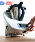 Hand justiert die Basis eines weißen Thermomix Geräts mit TM6 und TM5 Abzeichen.