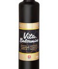 Eine hohe, schwarze Flasche mit goldfarbenem Schraubverschluss, die "Vita Balsamico" Balsamessig aus Apfel, Honig und Miele enthält. Das Etikett ist schwarz und gold mit einem Schweizer Kreuz und der Angabe "Swiss Made".