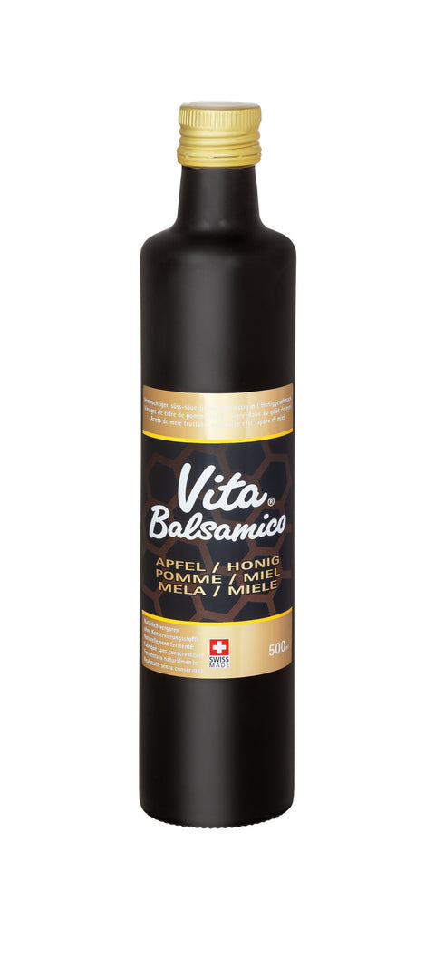 Eine hohe, schwarze Flasche mit goldfarbenem Schraubverschluss, die "Vita Balsamico" Balsamessig aus Apfel, Honig und Miele enthält. Das Etikett ist schwarz und gold mit einem Schweizer Kreuz und der Angabe "Swiss Made".